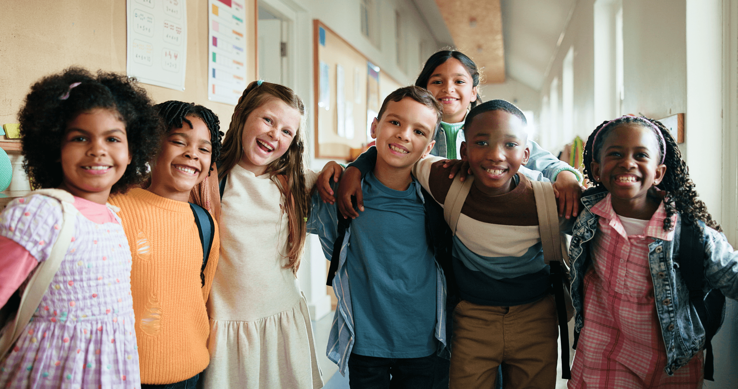 Six smiling students standing together in a school hallway